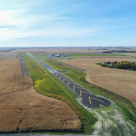 Aerial view of a rural runway with yellow lines, surrounded by fields.