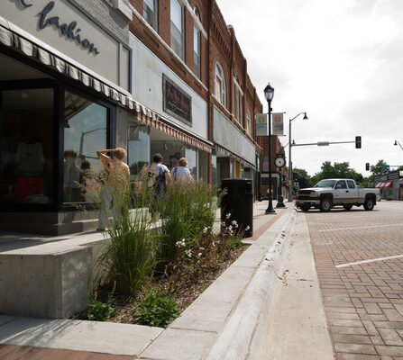 An active downtown featuring a mix of grassy elements in the surrounding landscape with parallel parking spots along the street