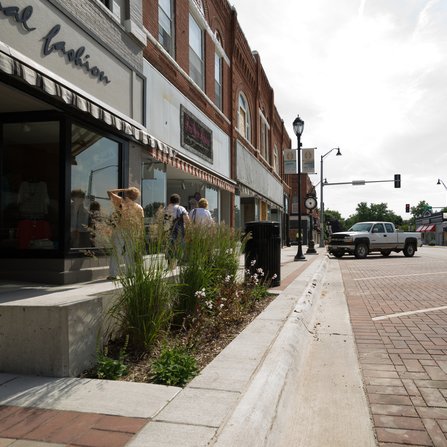 An active downtown featuring a mix of grassy elements in the surrounding landscape with parallel parking spots along the street