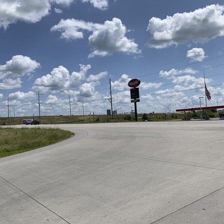 Road in front of gas station with power lines, under a blue sky with clouds