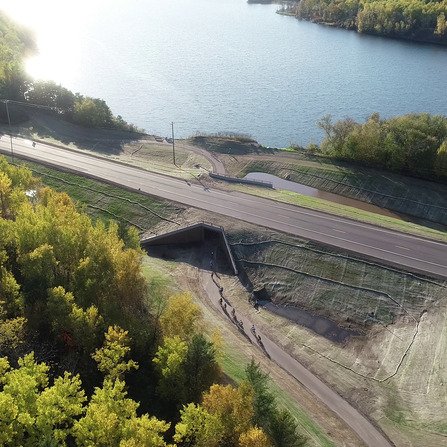 Arial view of bikers on a trail, passing through a tunnel beneath a highway.