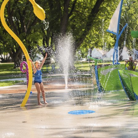 Children playing in a colorful community splash pad with various water features