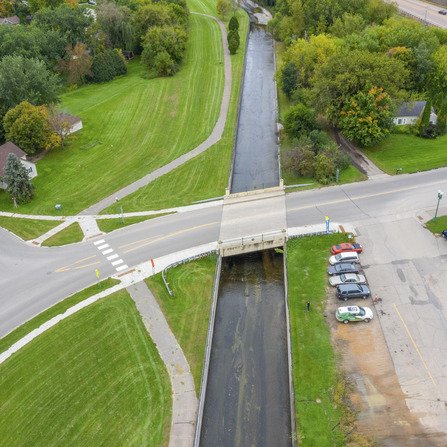 A bird's-eye view of a road intersection, featuring a bridge over a river, with roads and sidewalks