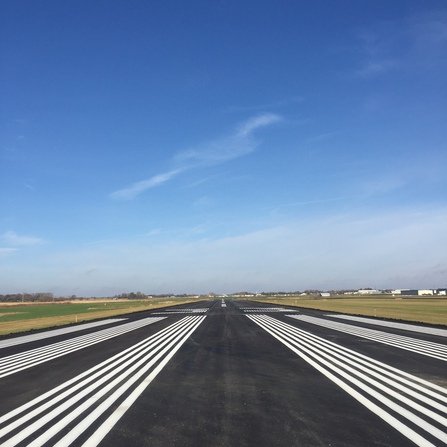 A detailed view of an airport runway, highlighting the white markings on the pavement