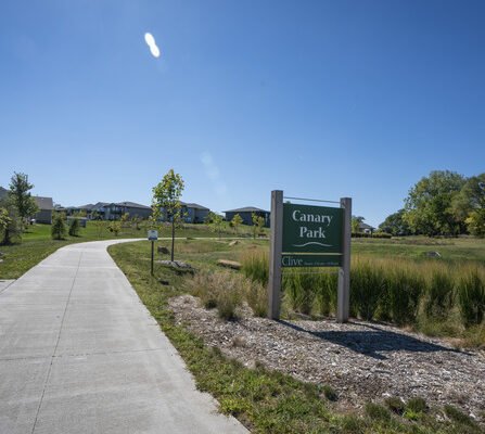 Sidewalk with bench and park sign in a residential area surrounded by native grass and trees