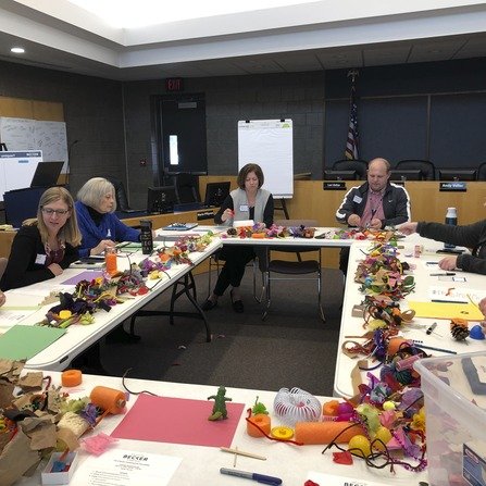 A group of individuals sitting around a table, working together and using craft materials to create visual aids