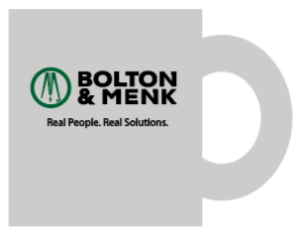 A white mug featuring the Bolton & Menk logo in black text with a green circle enclosing a stylized M. Below, the slogan reads Real People. Real Solutions. The mug is positioned handle to the right.